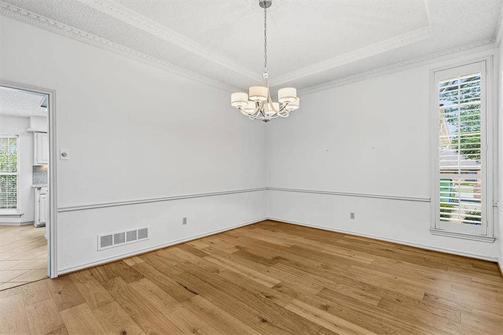 Room featuring wood-finish flooring, a coffered ceiling with crown molding, chair rail detailing, and a multi-arm chandelier with fabric shades