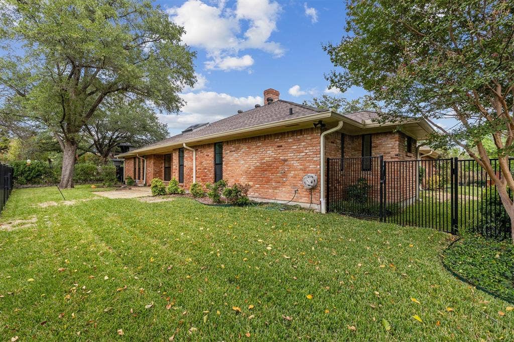 Exterior elevation featuring a red brick facade, chimney, fenced backyard, mature trees, and a concrete patio