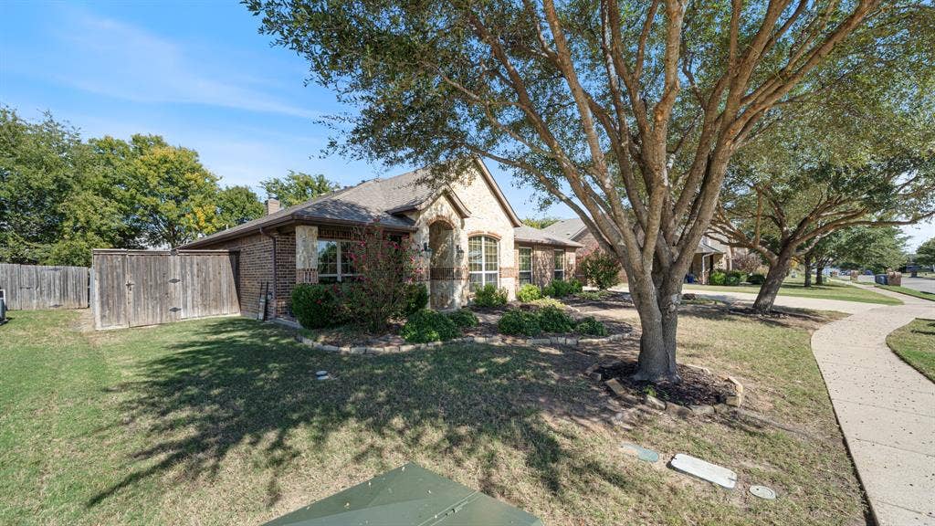 1802 Watermark Lane, Wylie, TX 75098 Brick exterior featuring a stone-accented arched entryway, mature shade trees, and wood-panel privacy fencing