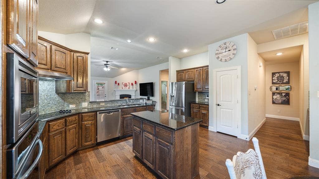 1802 Watermark Lane, Wylie, TX 75098 Kitchen featuring wood cabinetry, stone countertops, stainless steel appliances, a center island, and wood-finish flooring