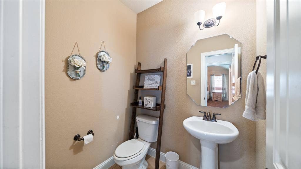 1802 Watermark Lane, Wylie, TX 75098 Powder room featuring a white porcelain pedestal sink with bronze-finish faucet, an octagonal wall mirror, and dual-light vanity fixture