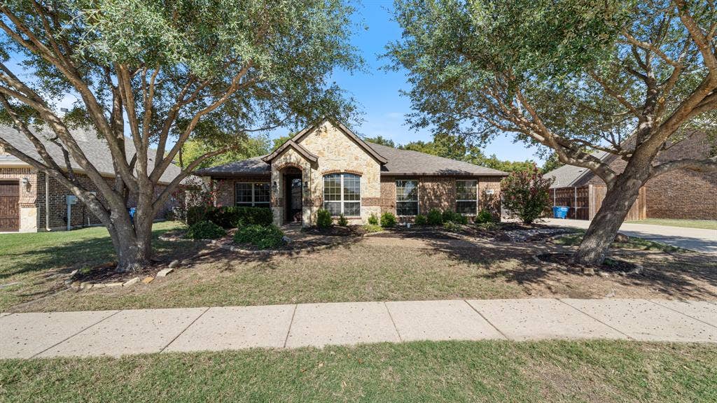 1802 Watermark Lane, Wylie, TX 75098 Single-story residence featuring a masonry exterior, multi-gable roofline, front-facing arched window, covered entryway, and mature shade trees