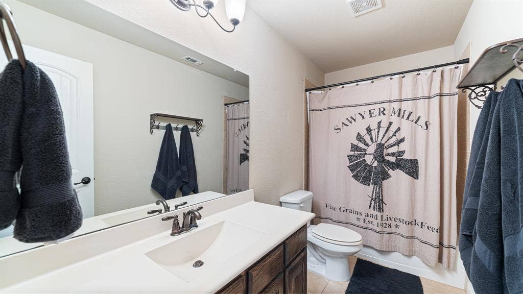 1802 Watermark Lane, Wylie, TX 75098 Bathroom featuring a vanity with an integrated sink, dark-toned cabinetry, a wide wall-mounted mirror, and a wall-mounted light fixture