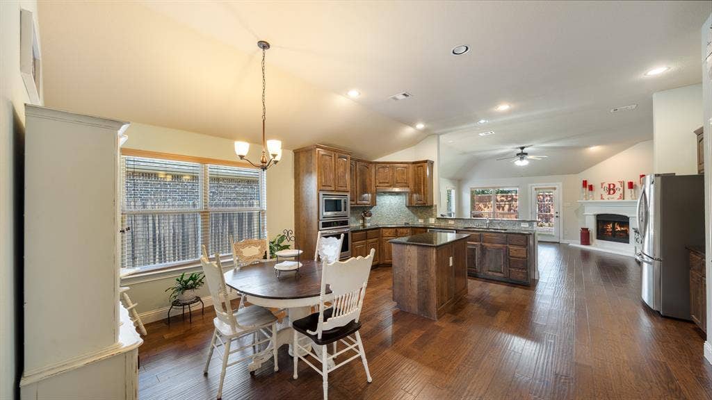 1802 Watermark Lane, Wylie, TX 75098 Kitchen featuring wood cabinetry, an island with stone countertops, built-in stainless steel appliances, wood-finish flooring, and a vaulted ceiling