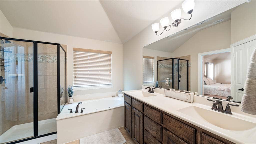 1802 Watermark Lane, Wylie, TX 75098 Bathroom featuring a dual-sink vanity with dark-finish cabinetry, a large wall-mounted mirror, a jetted soaking tub, and a separate glass-enclosed shower with tiled surround