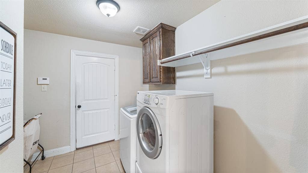 1802 Watermark Lane, Wylie, TX 75098 Laundry area featuring ceramic tile flooring, upper wood cabinetry, and a wall-mounted shelving unit with an integrated hanging rod