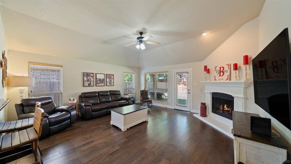 1802 Watermark Lane, Wylie, TX 75098 Living area featuring vaulted ceilings, wood-finish flooring, a fireplace with a decorative mantel, and a ceiling fan