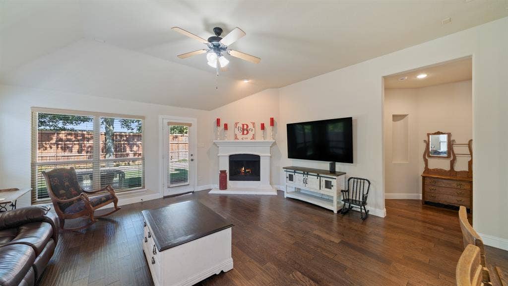 1802 Watermark Lane, Wylie, TX 75098 Vaulted ceilings, wood-finish flooring, corner fireplace with white mantle, and recessed wall niche