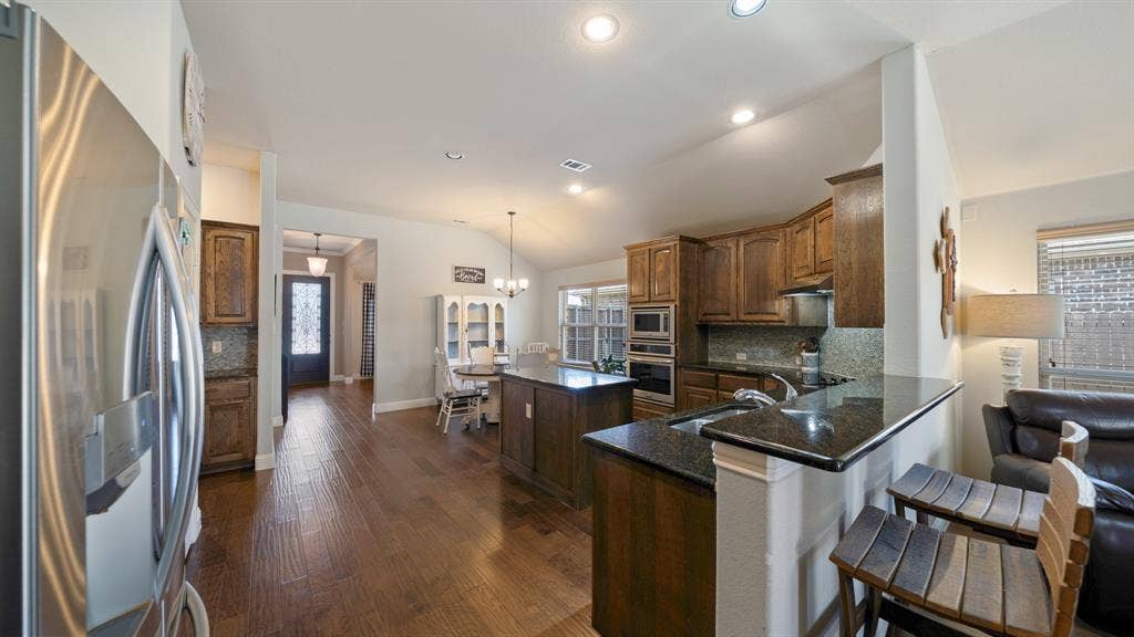 1802 Watermark Lane, Wylie, TX 75098 Kitchen featuring wood cabinetry, stone countertops, stainless steel appliances, a center island, and wood-finish flooring