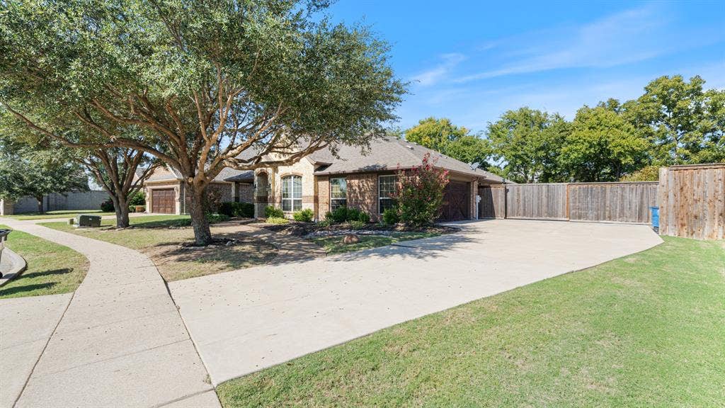 1802 Watermark Lane, Wylie, TX 75098 Single-story masonry exterior featuring a concrete driveway, a wood privacy fence, and mature trees on a landscaped lot
