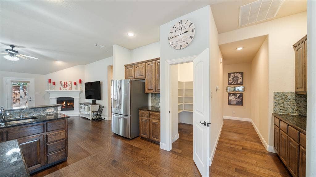 1802 Watermark Lane, Wylie, TX 75098 Kitchen featuring wood cabinetry, stone countertops, a walk-in pantry, and wood-finish flooring, complemented by a gas fireplace with a mantel