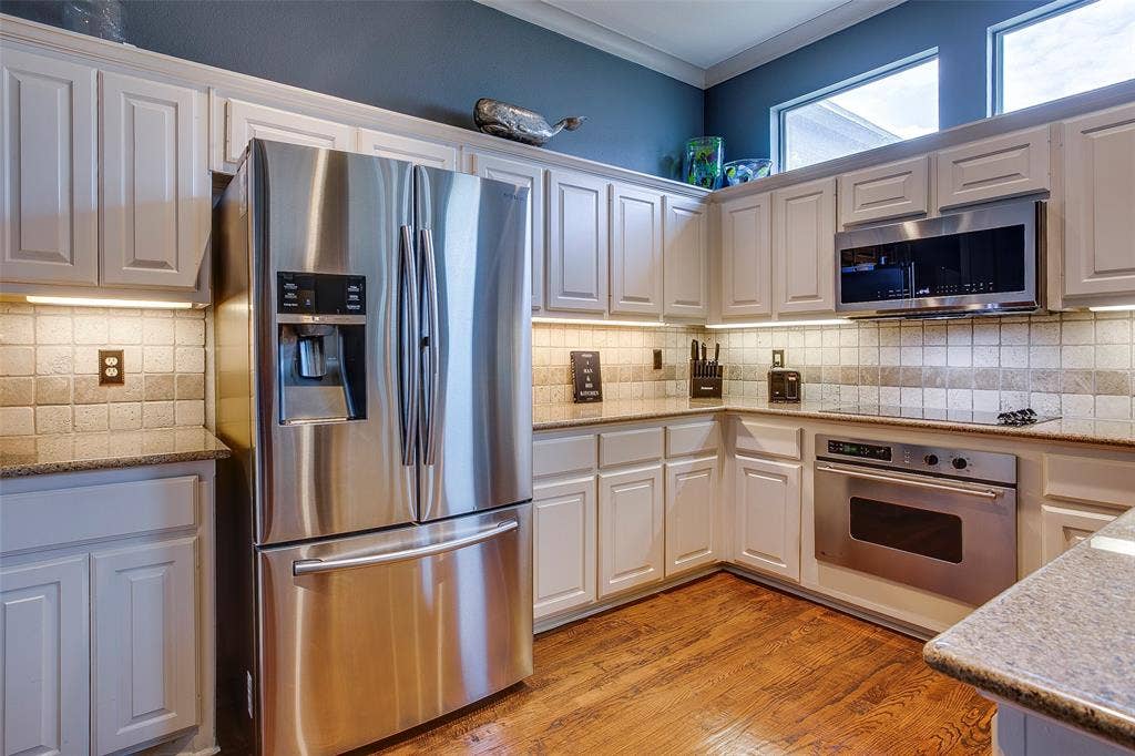 Kitchen featuring white paneled cabinetry, stainless steel appliances, granite countertops, and a tiled backsplash