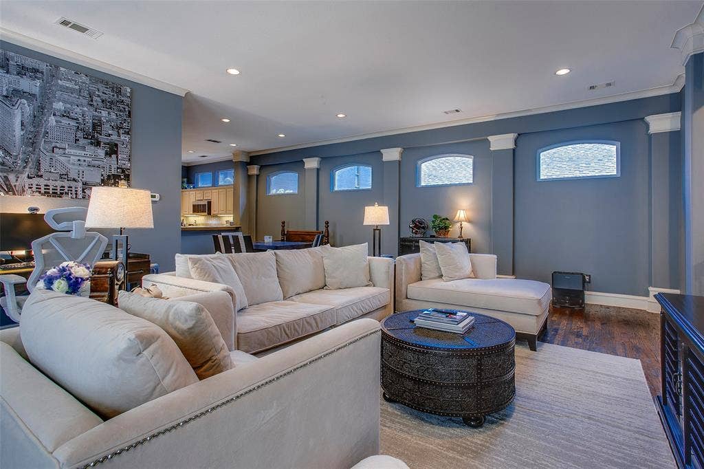 Spacious living area featuring recessed lighting, crown molding, arched transom windows, dark wood-finish flooring, and a partial view of a kitchen with wood cabinetry