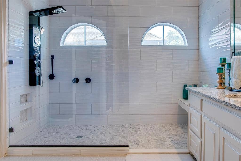 Glass-enclosed shower with a multi-function shower panel, integrated wall niches, and pebble-style floor tiling
