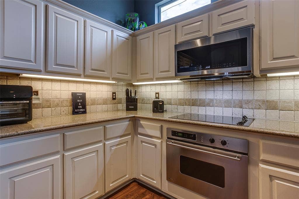 Kitchen featuring light-toned cabinetry, a built-in stainless steel microwave, and a smooth-top electric cooktop