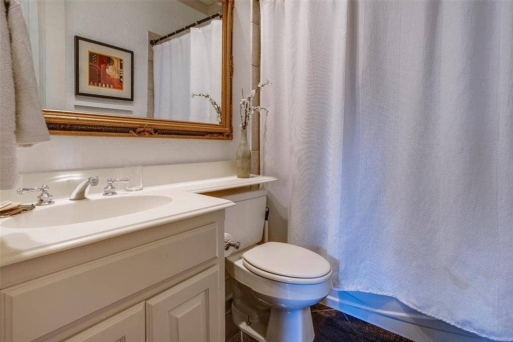 White vanity with a polished chrome faucet, an ornate gold-framed mirror, and a built-in shelf above the toilet