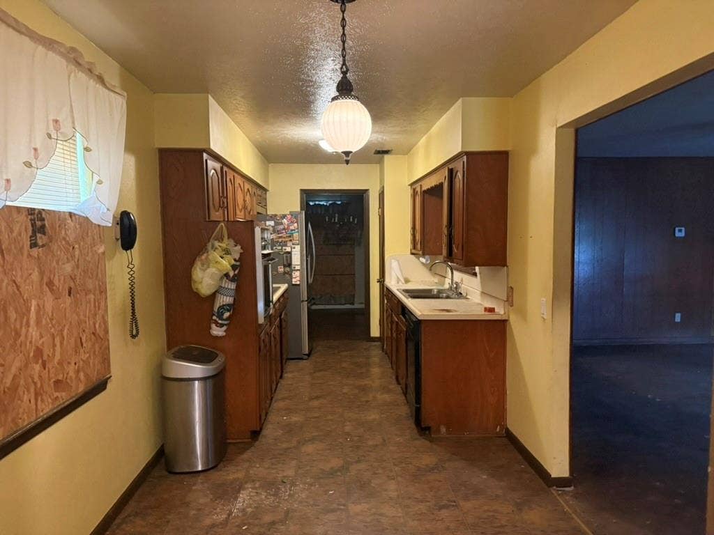 Galley kitchen featuring wood cabinetry, integrated oven, double-basin sink, and globe pendant lighting