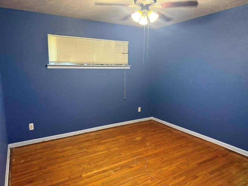Room featuring wood-finish flooring, a ceiling-mounted light fixture with a fan, and a horizontal window with adjustable blinds