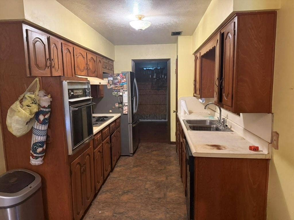 Kitchen featuring wood cabinetry, integrated wall oven, countertop stove, double-basin stainless steel sink, and resilient flooring