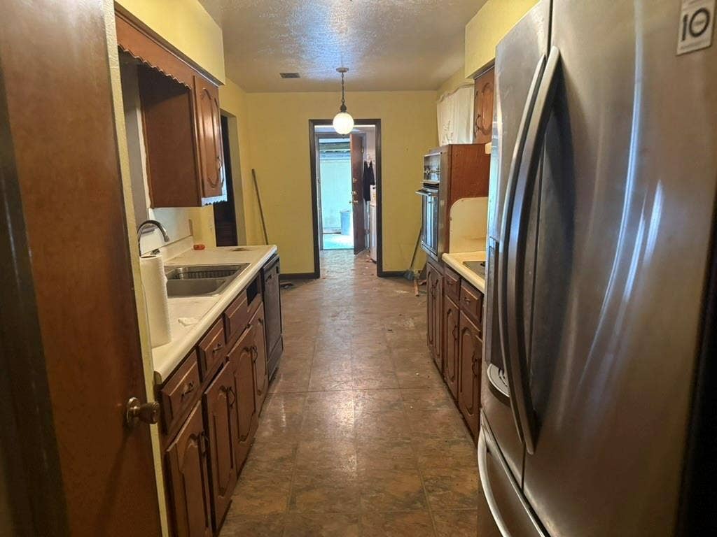 Galley kitchen featuring wood-finish cabinetry, solid-surface countertops, integrated stainless steel oven, and tile flooring