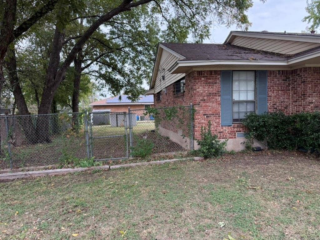 Brick exterior siding with window shutters, chain-link perimeter fencing, and mature trees