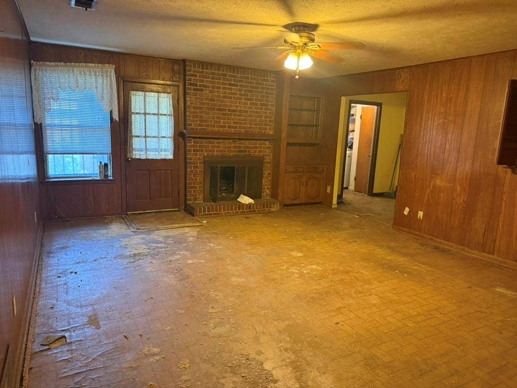 Interior room featuring wood-paneled walls, brick fireplace with a raised hearth, built-in cabinetry, and a ceiling fan with integrated light fixture