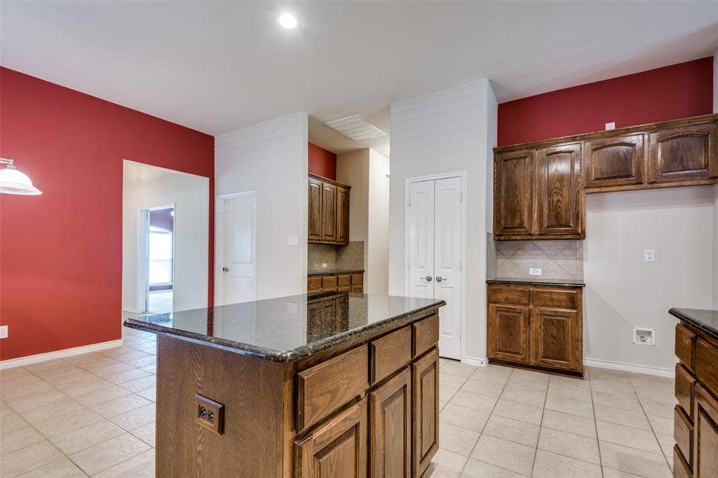 Kitchen featuring tasteful backsplash, baseboards, dark stone countertops, light tile patterned floors, and a center island