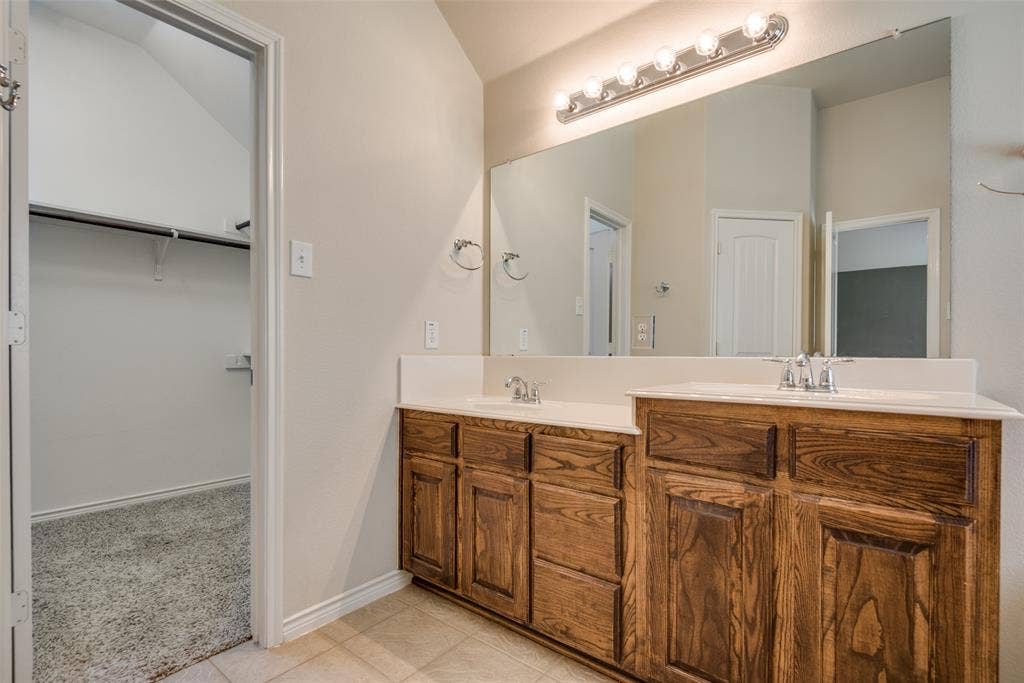 Bathroom with baseboards, a sink, a walk in closet, double vanity, and tile patterned floors