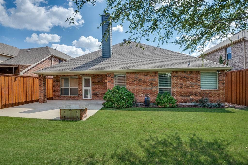 Rear view of house featuring roof with shingles, a patio area, fence, and a lawn