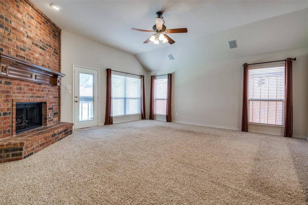 Unfurnished living room with visible vents, a brick fireplace, a ceiling fan, vaulted ceiling, and carpet flooring