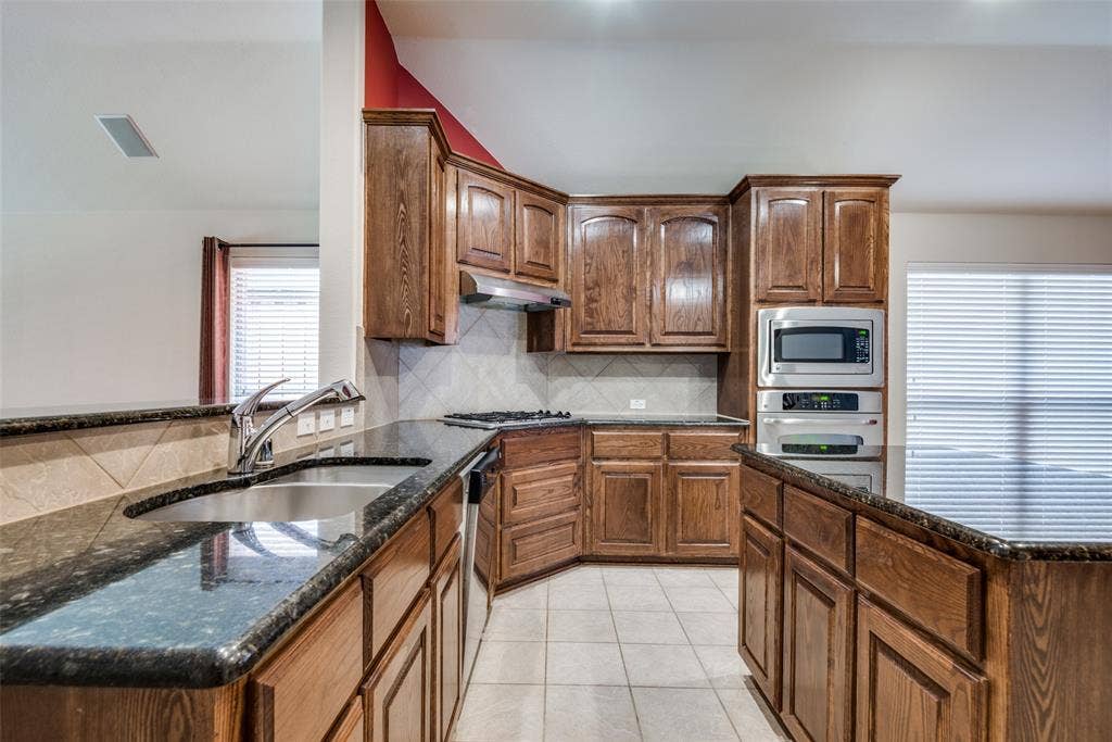 Kitchen featuring light tile patterned floors, under cabinet range hood, a sink, lofted ceiling, and stainless steel appliances