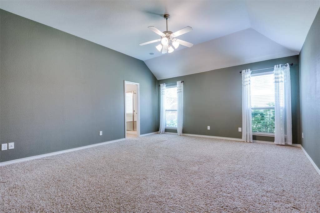 Carpeted spare room featuring a healthy amount of sunlight, ceiling fan, baseboards, and lofted ceiling
