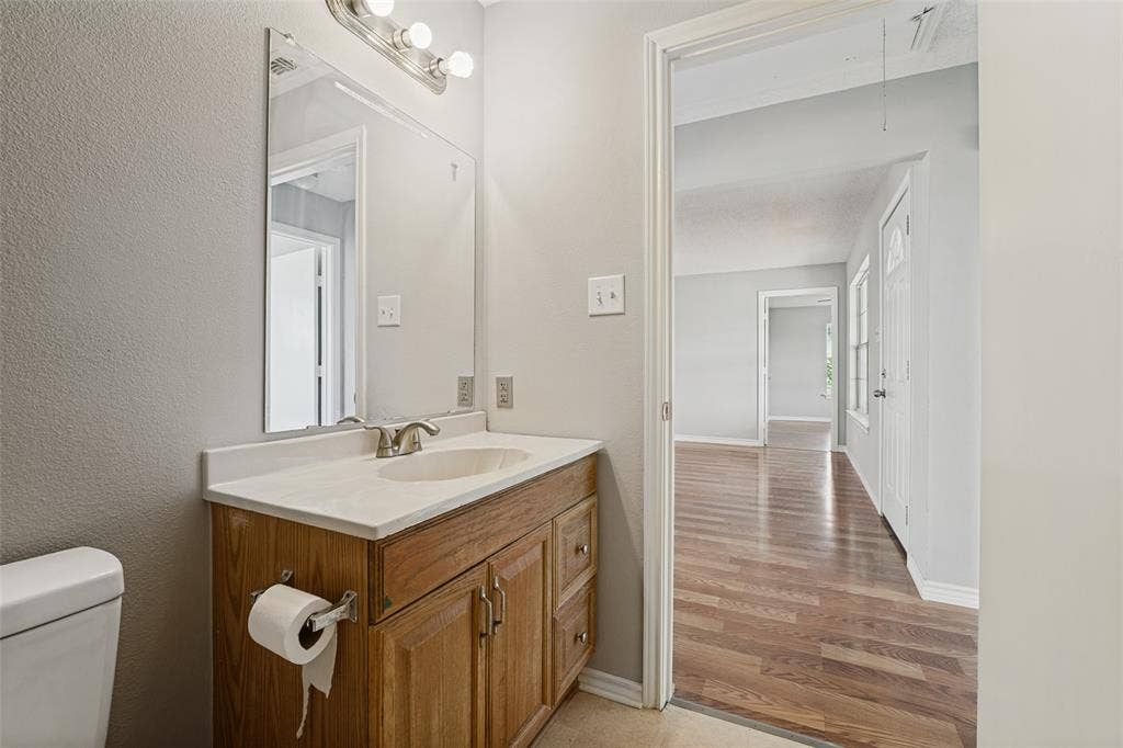 415 S Bell Street, Royse City, TX 75189 Bathroom featuring a wood-finish vanity with a rectangular sink, solid surface countertop, polished chrome faucet, and a large wall-mounted mirror with integrated lighting