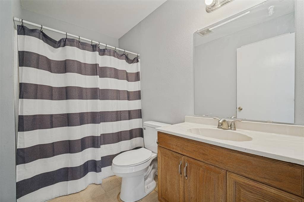 415 S Bell Street, Royse City, TX 75189 Bathroom featuring a wood-finish vanity with an integrated basin, a large wall-mounted mirror, overhead vanity lighting, and a bathtub with a curtain rod