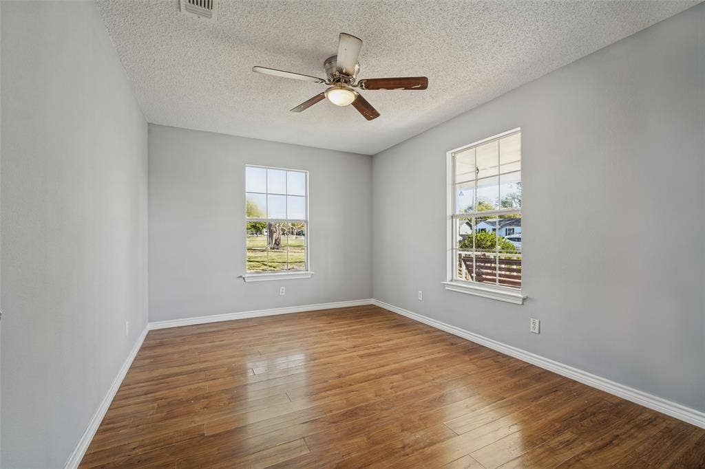 415 S Bell Street, Royse City, TX 75189 Room featuring wood-finish flooring, dual windows with grid detailing, and a central ceiling fan with integrated lighting