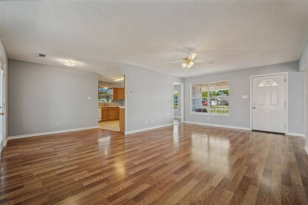 415 S Bell Street, Royse City, TX 75189 Open interior space featuring wood-finish flooring, a ceiling-mounted fan, multiple windows with grid detailing, and a paneled entry door