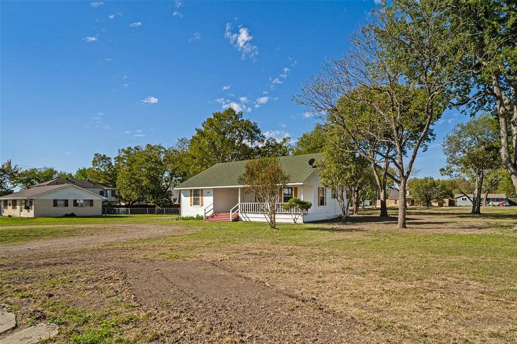 415 S Bell Street, Royse City, TX 75189 Single-story home featuring a covered front porch with white railing, exterior shutters, and a sloped roof set on a large lot with mature trees