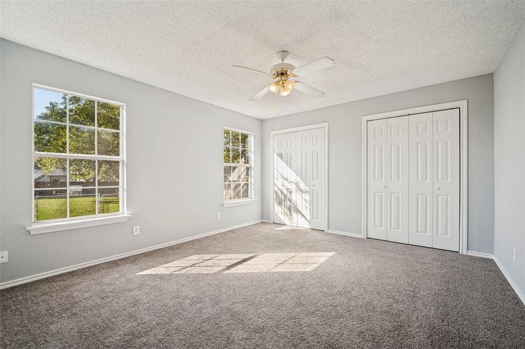 415 S Bell Street, Royse City, TX 75189 Neutral-toned interior featuring wall-to-wall carpeting, dual double-door closets, multiple pane windows, and a ceiling-mounted fan with integrated lighting