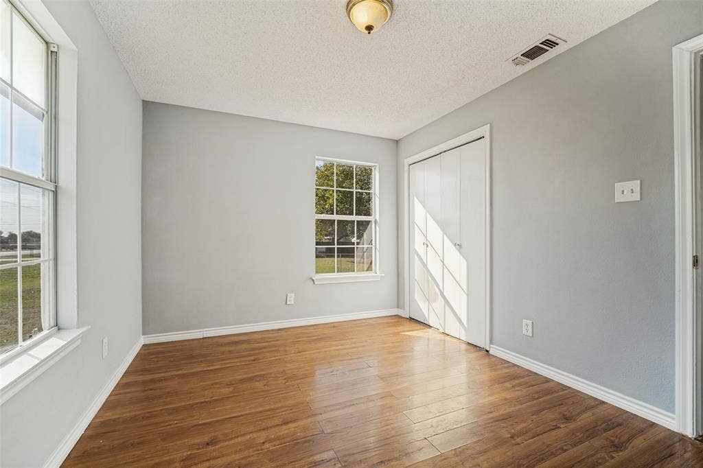 415 S Bell Street, Royse City, TX 75189 Room featuring wood-finish flooring, dual windows with grid detailing, neutral-toned wall paint, and a built-in closet with double doors