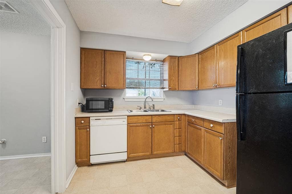 415 S Bell Street, Royse City, TX 75189 Kitchen featuring wood cabinetry, solid-surface countertops, dual-basin stainless steel sink, and light-toned tile flooring