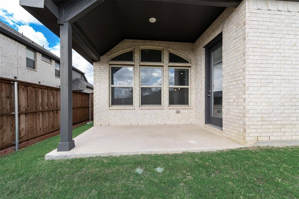 3934 Timberview Street, Midlothian, TX 76065 Covered concrete patio featuring a light-colored brick exterior, arched-top windows, and a wood privacy fence