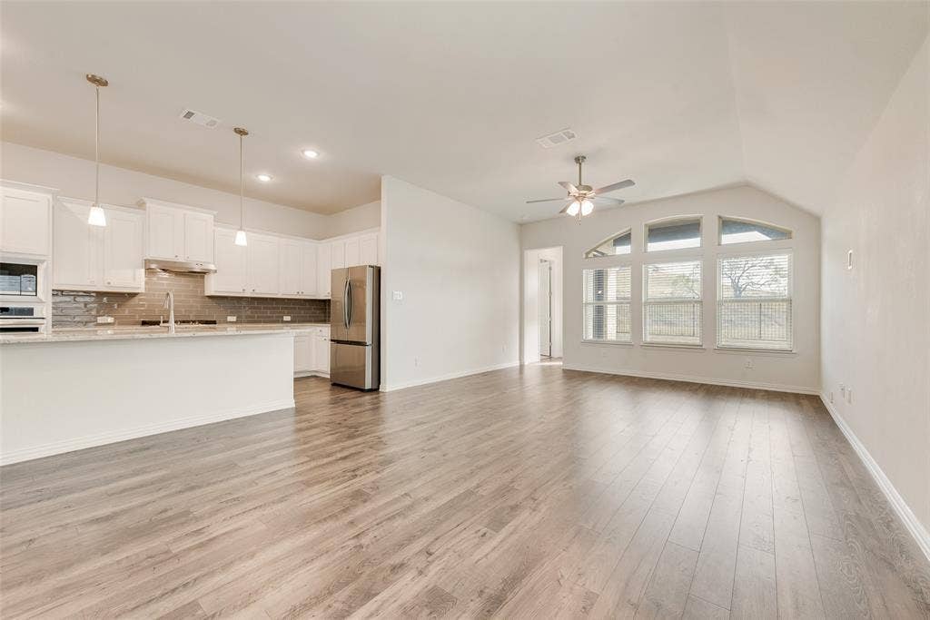 3934 Timberview Street, Midlothian, TX 76065 Open-concept interior featuring wood-finish flooring, vaulted ceilings, white cabinetry, stainless steel appliances, and arched windows