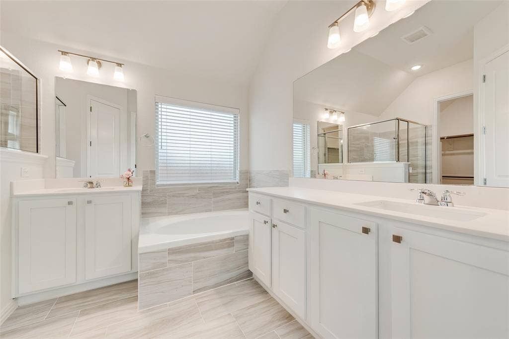 3934 Timberview Street, Midlothian, TX 76065 Dual white vanities with light-toned countertops, oversized wall-to-wall vanity mirrors, deep soaking tub with tile surround, and neutral large-format tile flooring