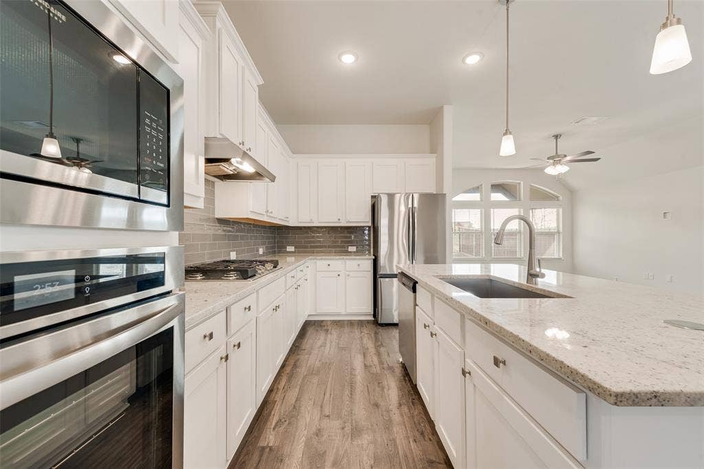 3934 Timberview Street, Midlothian, TX 76065 Kitchen featuring white shaker cabinetry, stone-finish countertops, stainless steel appliances including a built-in wall oven and microwave, gray subway tile backsplash, and wood-finish flooring