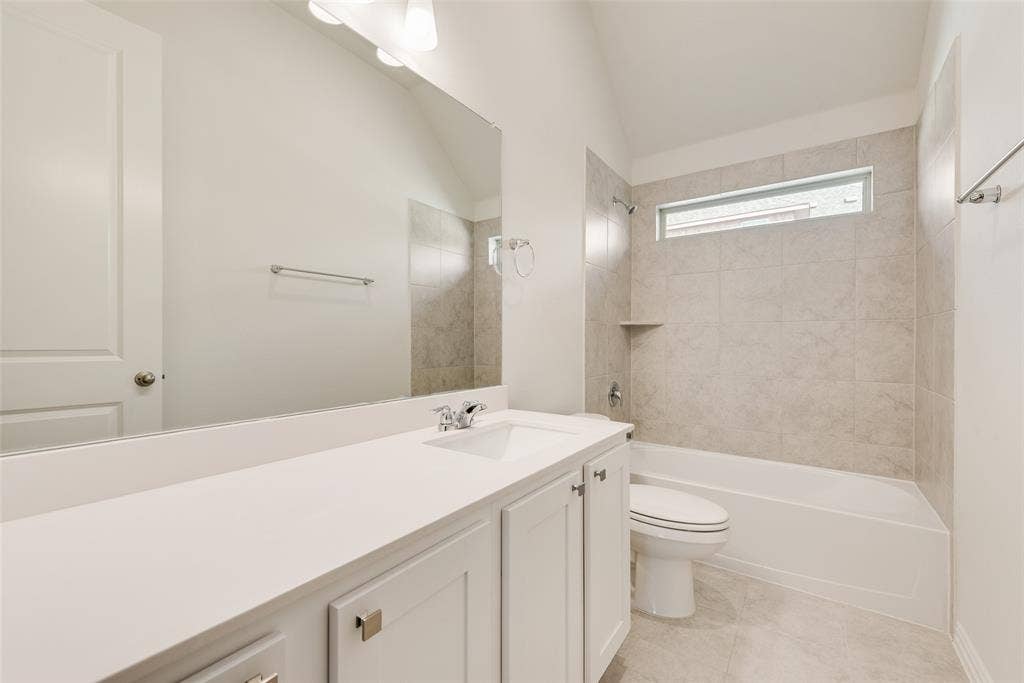 3934 Timberview Street, Midlothian, TX 76065 Vanity with a solid surface countertop, rectangular under-mount sink, oversized wall mirror, vaulted ceiling, and a porcelain tile shower surround with integrated shelving