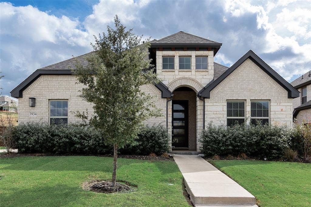 3934 Timberview Street, Midlothian, TX 76065 Exterior facade featuring light-colored stone masonry, a covered arched entryway, a multi-pane glass panel front door, and a multi-gabled roofline