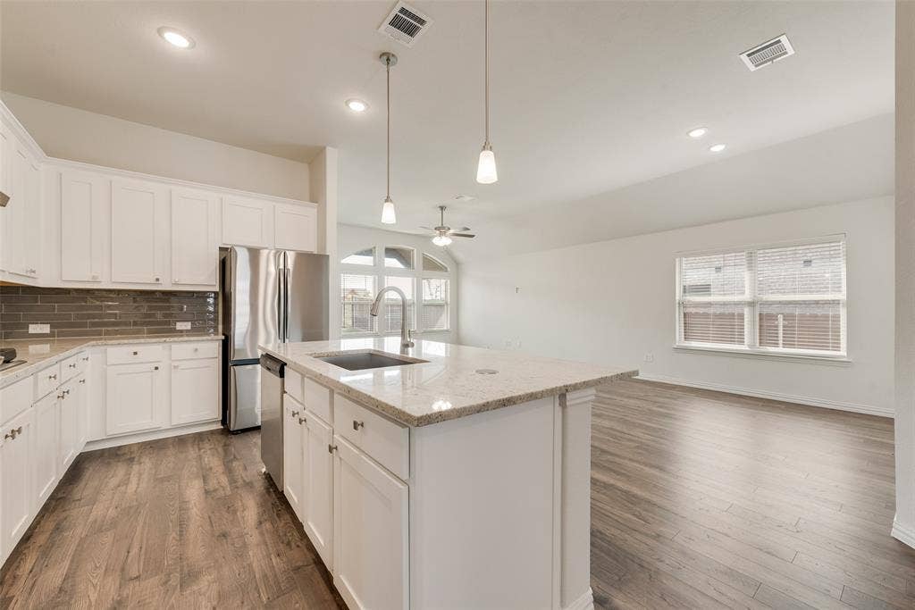 3934 Timberview Street, Midlothian, TX 76065 Kitchen featuring white cabinetry, stone-surface island with integrated sink, stainless steel refrigerator, tile backsplash, and wood-finish flooring