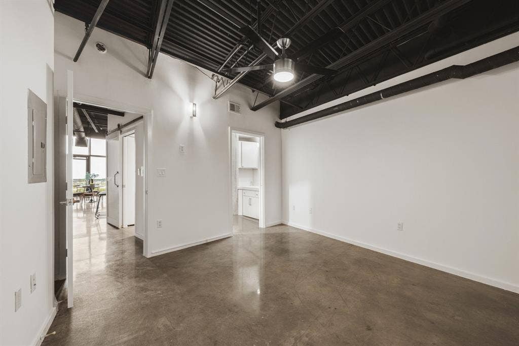 3110 Thomas Avenue, #717, Dallas, TX 75204 Exposed ceiling beams, industrial-style ceiling fan, polished concrete flooring, white walls, and contemporary wall sconce
