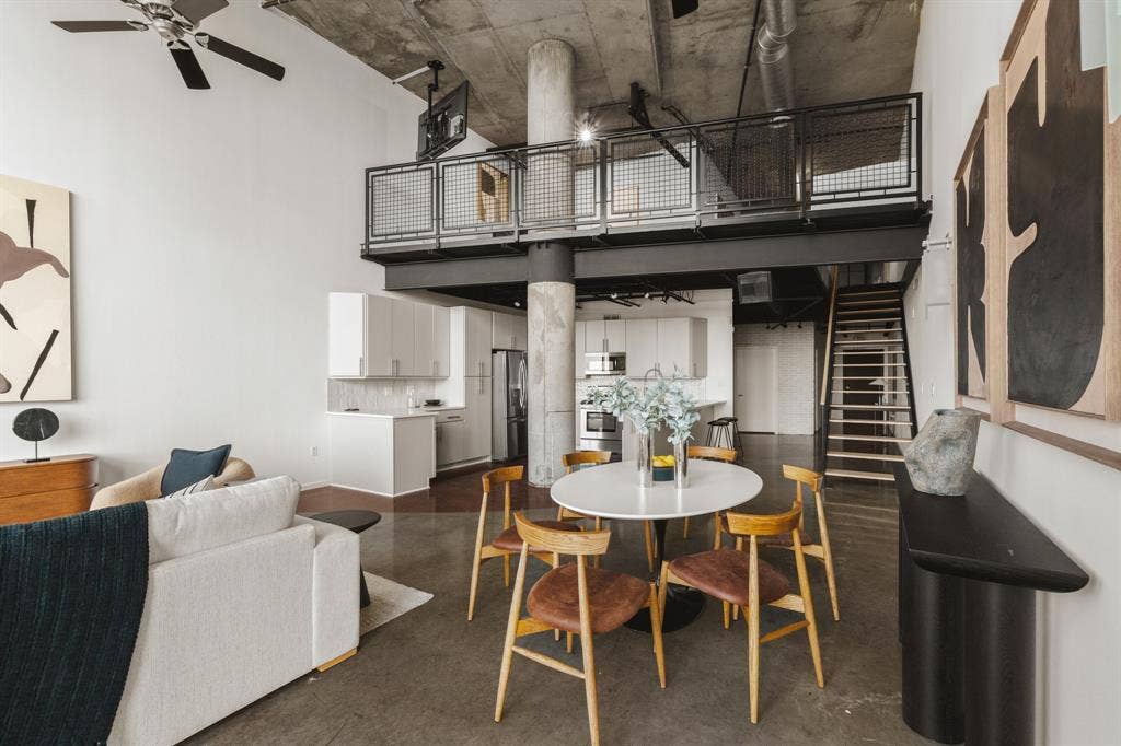 3110 Thomas Avenue, #717, Dallas, TX 75204 High ceilings with exposed concrete, polished concrete flooring, open-concept kitchen with white cabinetry, and an upper-level mezzanine with metal railing