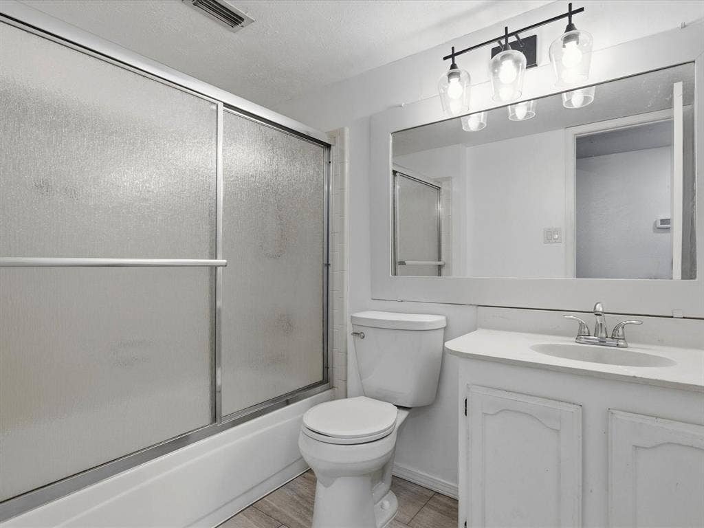 Bathroom featuring a vanity with integrated sink, full-width mirror, three-light fixture, and tub with a sliding glass enclosure